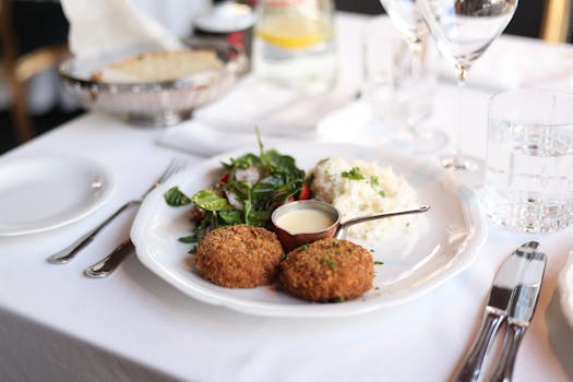 Assiette blanche avec deux croquettes dorées, salade verte, purée de pommes de terre et sauce dans un petit récipient.