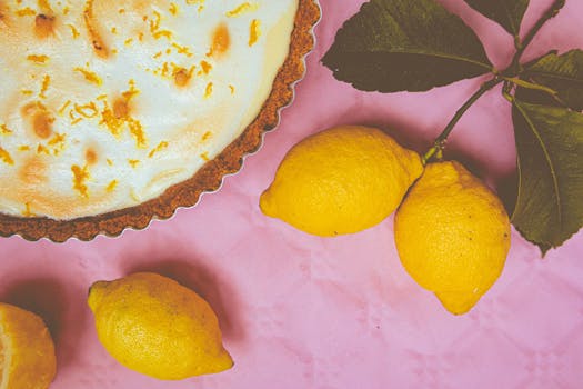 Tarte au citron avec une croûte dorée, accompagnée de citrons frais sur un fond rose.