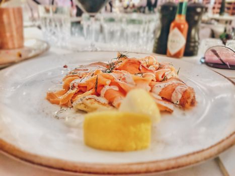 Assiette de saumon fumé avec sauce crémeuse et un quartier de citron sur un fond flou.